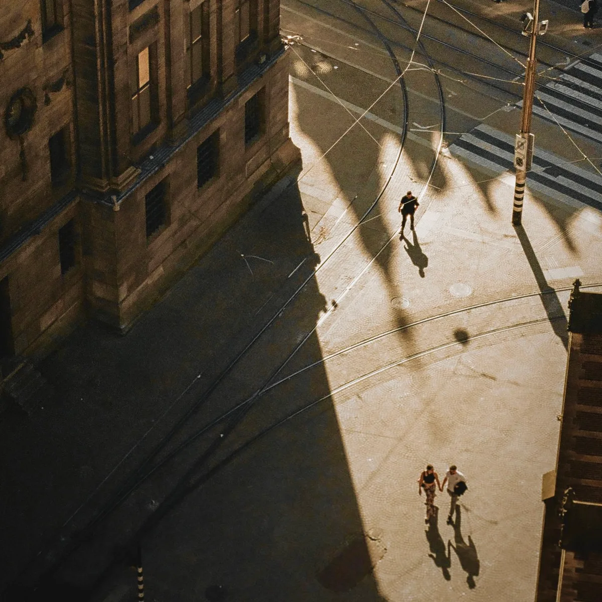 Long afternoon shadows of buildings falling across a city street and pedestrians